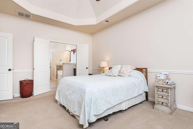 carpeted bedroom with a raised ceiling and connected bathroom