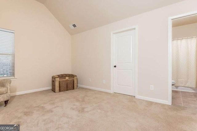 unfurnished bedroom with vaulted ceiling, light colored carpet, and ensuite bath