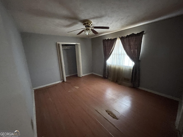 unfurnished bedroom with ceiling fan, a closet, wood-type flooring, and a textured ceiling