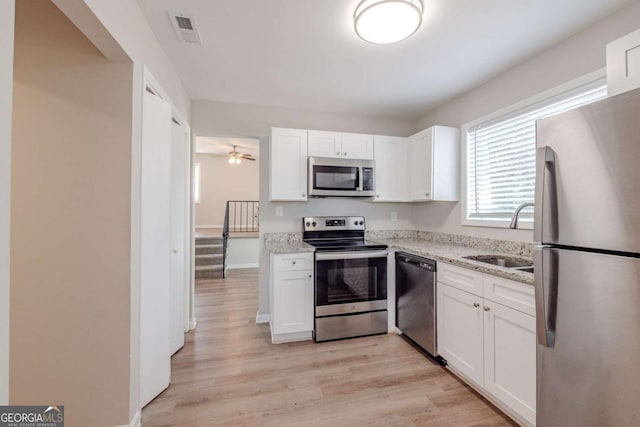 kitchen with light stone counters, stainless steel appliances, ceiling fan, sink, and white cabinetry