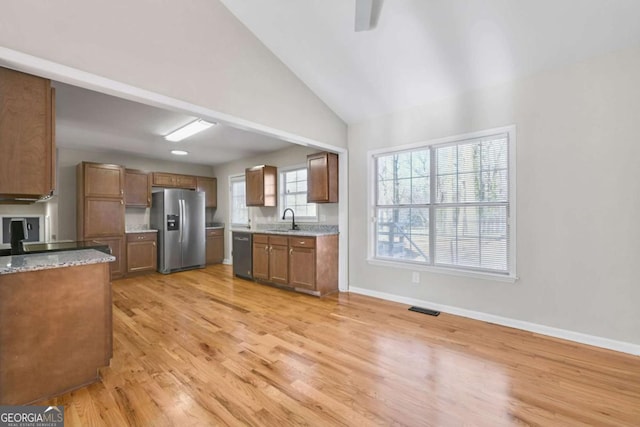 kitchen with light stone countertops, sink, stainless steel appliances, high vaulted ceiling, and light hardwood / wood-style floors