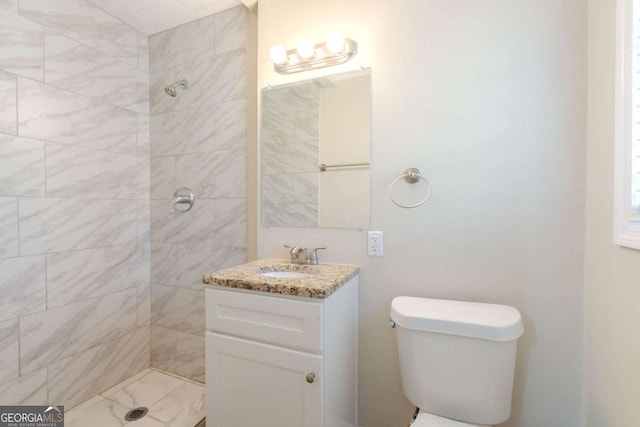 bathroom with a tile shower, vanity, and toilet