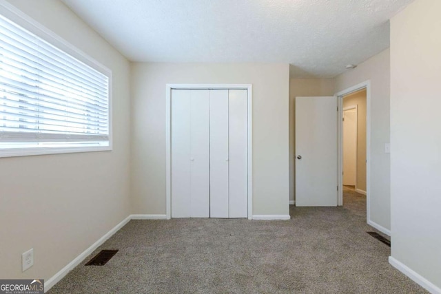 unfurnished bedroom with light colored carpet, a textured ceiling, and a closet