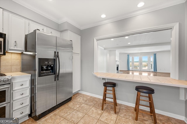 kitchen featuring tile counters, a breakfast bar, white cabinetry, and stainless steel appliances