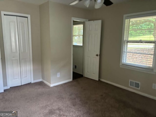 unfurnished bedroom with dark colored carpet, a closet, and ceiling fan