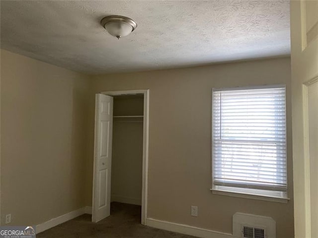 unfurnished bedroom featuring a textured ceiling, dark carpet, and a closet