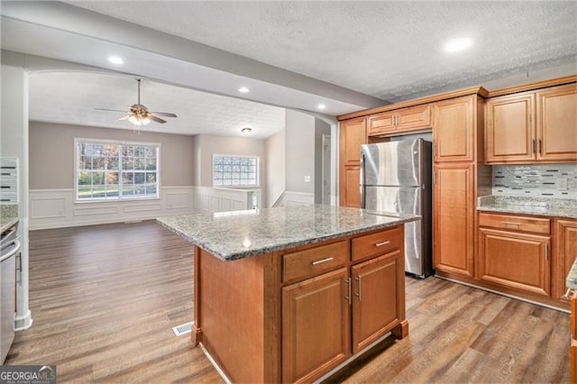 kitchen featuring stainless steel fridge, a center island, light stone counters, and light hardwood / wood-style floors