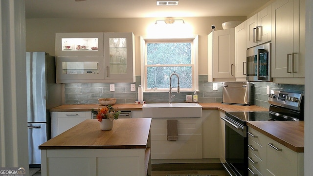 kitchen featuring backsplash, butcher block counters, white cabinetry, and stainless steel appliances