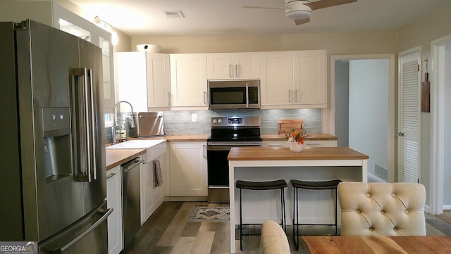 kitchen featuring wood counters, stainless steel appliances, white cabinetry, and tasteful backsplash