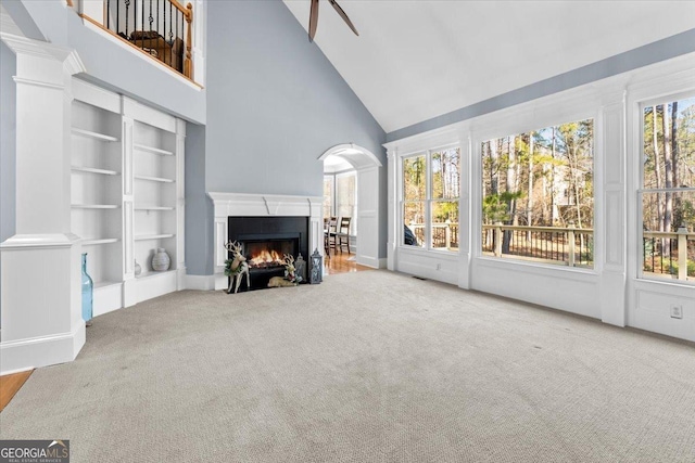 unfurnished living room with high vaulted ceiling, built in features, a wealth of natural light, and carpet floors