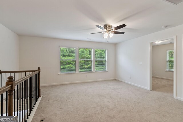 spare room with light colored carpet, a wealth of natural light, and ceiling fan