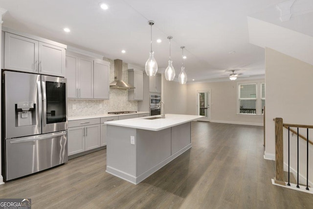 kitchen with a kitchen island with sink, wall chimney range hood, ceiling fan, appliances with stainless steel finishes, and decorative light fixtures