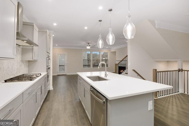 kitchen featuring sink, hanging light fixtures, wall chimney range hood, a center island with sink, and appliances with stainless steel finishes