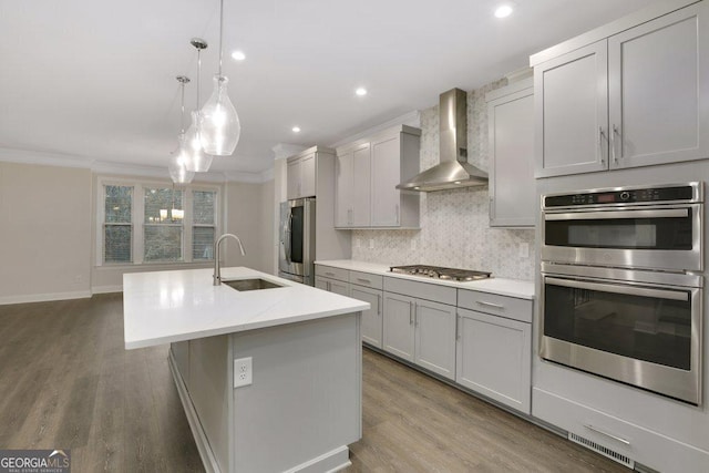 kitchen with gray cabinetry, sink, wall chimney exhaust hood, stainless steel appliances, and hanging light fixtures