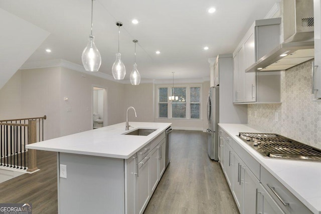 kitchen with sink, wall chimney exhaust hood, crown molding, pendant lighting, and a center island with sink