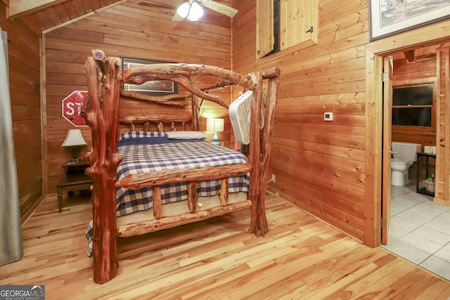 bedroom with ceiling fan, ensuite bathroom, vaulted ceiling, wooden walls, and light wood-type flooring