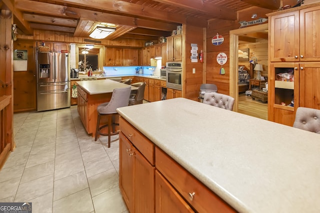 kitchen featuring wood walls, light tile patterned floors, beamed ceiling, wood ceiling, and stainless steel appliances