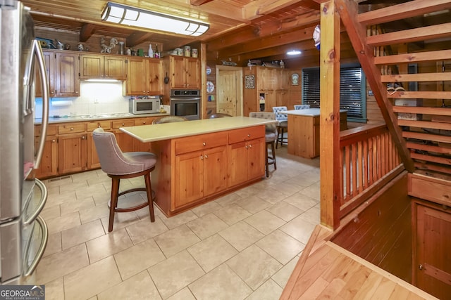 kitchen with a kitchen bar, appliances with stainless steel finishes, backsplash, light tile patterned floors, and a kitchen island