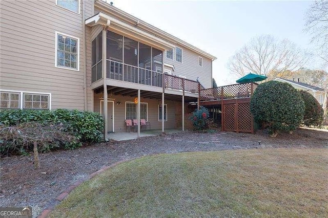 back of house featuring a patio, a lawn, a wooden deck, and a sunroom