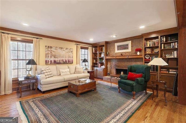 living room featuring built in shelves, ornamental molding, wood-type flooring, and a brick fireplace