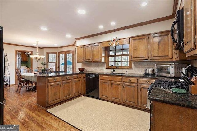 kitchen featuring a notable chandelier, kitchen peninsula, light hardwood / wood-style floors, decorative light fixtures, and black appliances