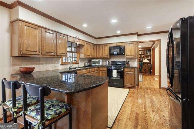 kitchen featuring kitchen peninsula, a breakfast bar, sink, black appliances, and light hardwood / wood-style floors