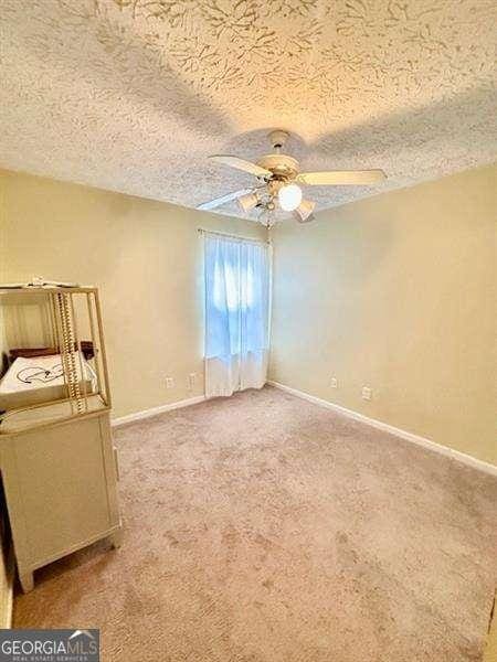 unfurnished bedroom with ceiling fan, carpet floors, and a textured ceiling