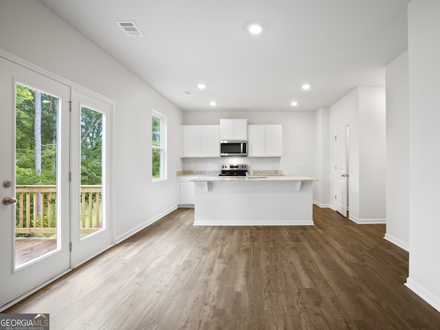 kitchen featuring white cabinets, appliances with stainless steel finishes, a kitchen island with sink, and wood-type flooring