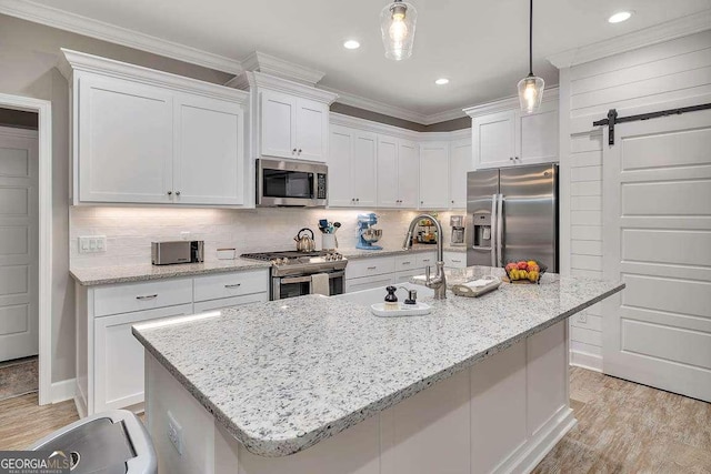 kitchen featuring white cabinets, a barn door, stainless steel appliances, and hanging light fixtures