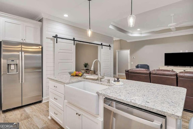 kitchen with white cabinets, a center island with sink, a barn door, appliances with stainless steel finishes, and a tray ceiling