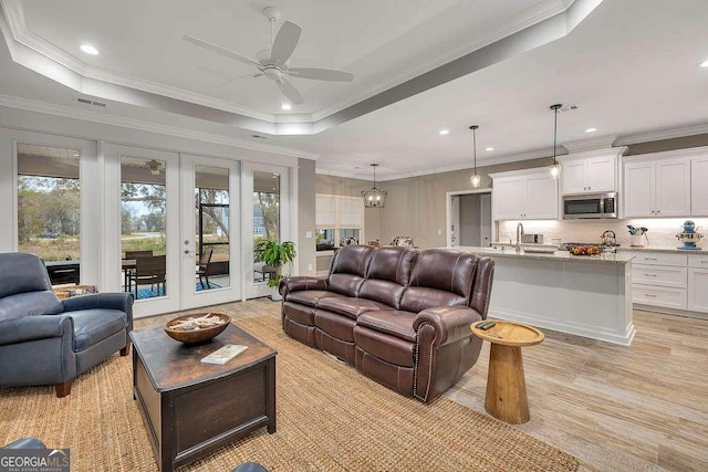 living room featuring a raised ceiling, crown molding, french doors, and ceiling fan with notable chandelier