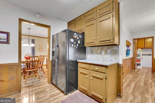 kitchen featuring an inviting chandelier, hanging light fixtures, light hardwood / wood-style flooring, decorative backsplash, and black fridge with ice dispenser