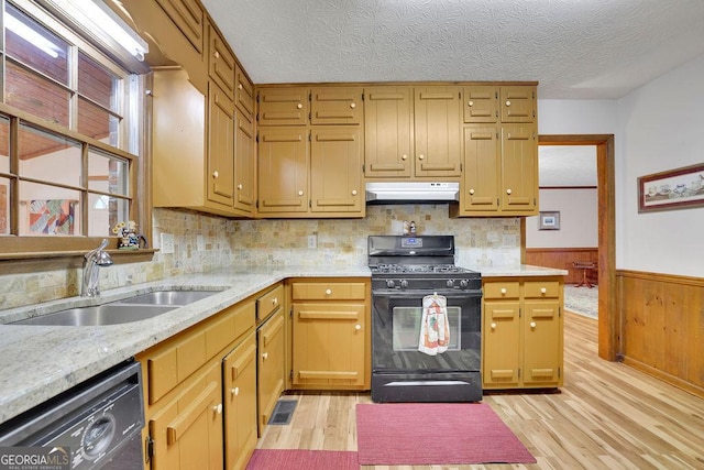 kitchen featuring dishwasher, sink, wooden walls, light hardwood / wood-style floors, and gas stove