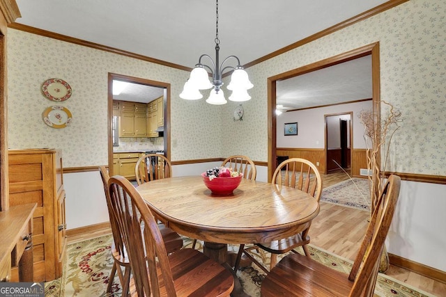 dining space with wood walls, light wood-type flooring, ornamental molding, and a notable chandelier