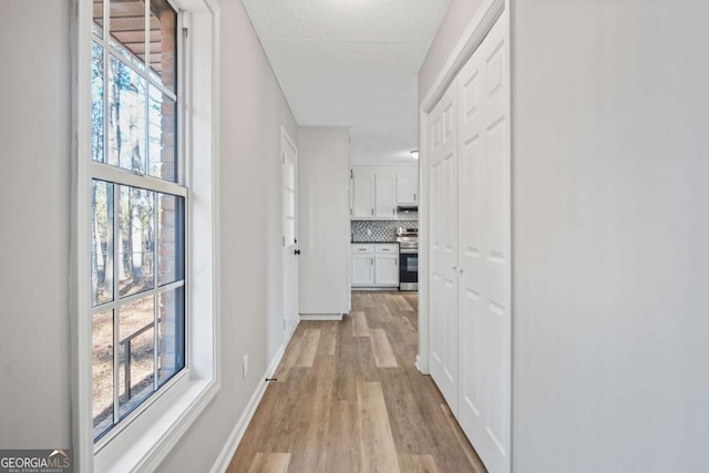 hallway with light wood-type flooring and a textured ceiling