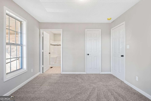 unfurnished bedroom with a textured ceiling, ensuite bathroom, and light carpet