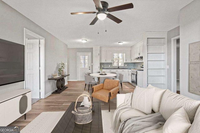 living room featuring light wood-type flooring, a textured ceiling, and ceiling fan