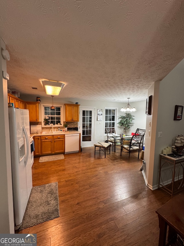 kitchen with pendant lighting, hardwood / wood-style floors, white appliances, an inviting chandelier, and a textured ceiling