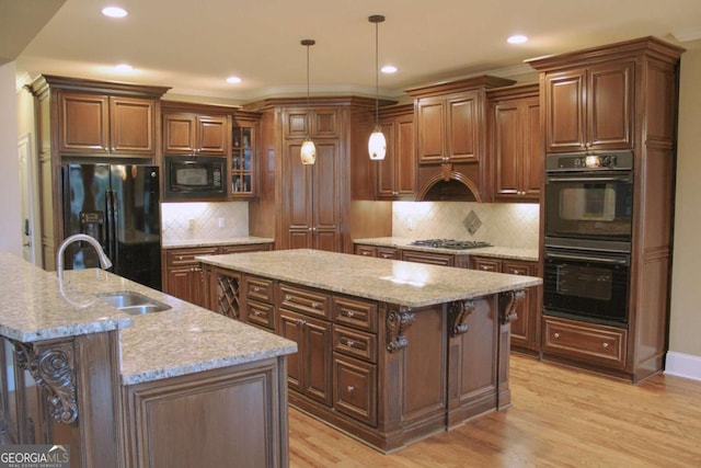 kitchen featuring pendant lighting, a center island with sink, black appliances, light hardwood / wood-style flooring, and light stone counters