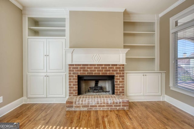 unfurnished living room featuring built in shelves, ornamental molding, light hardwood / wood-style floors, and a brick fireplace