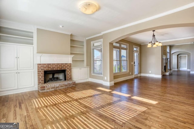 unfurnished living room with a fireplace, ornamental molding, wood-type flooring, built in features, and a chandelier