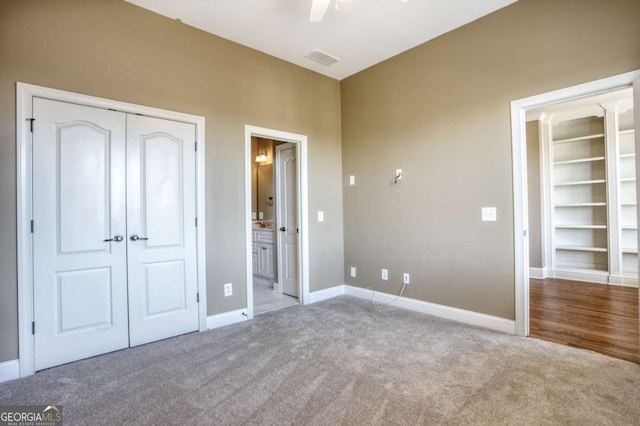 unfurnished bedroom with ceiling fan, a closet, ensuite bathroom, and light carpet