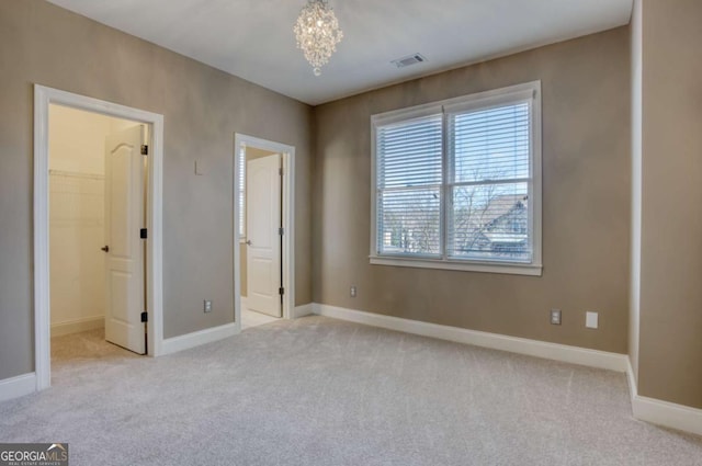 unfurnished bedroom featuring light colored carpet, a spacious closet, a closet, and a notable chandelier