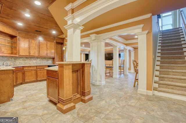 kitchen with decorative backsplash, a kitchen bar, ornate columns, and crown molding