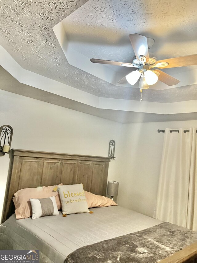 bedroom with ceiling fan, a raised ceiling, and a textured ceiling