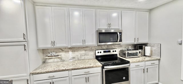 kitchen featuring decorative backsplash, light stone countertops, white cabinetry, and appliances with stainless steel finishes