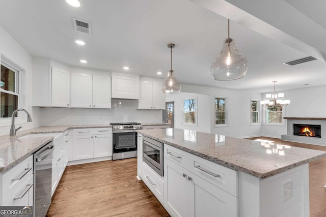 kitchen featuring a center island, a brick fireplace, decorative light fixtures, white cabinets, and appliances with stainless steel finishes