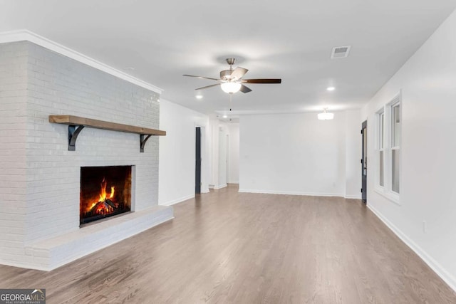 unfurnished living room with light hardwood / wood-style flooring, a brick fireplace, ceiling fan, and crown molding