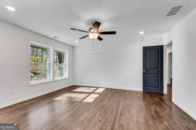 empty room with dark hardwood / wood-style floors, ceiling fan, and brick wall