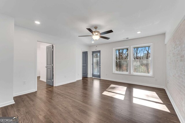 empty room with dark hardwood / wood-style floors, ceiling fan, and brick wall